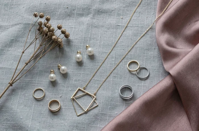 Flat lay de bijoux tendance Etam sur lin texturé, boucles d'oreilles perles, collier doré pendentif géométrique et bagues minimalistes