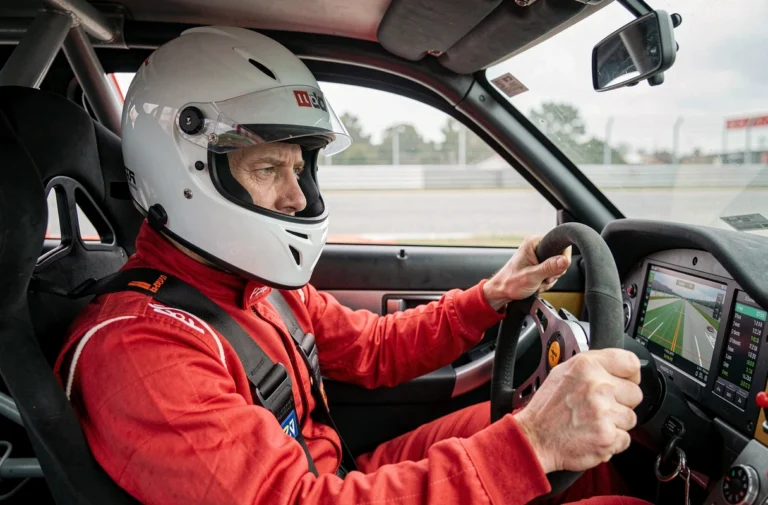 Pilote en combinaison rouge concentré au volant d'une voiture de course lors d'un stage de pilotage